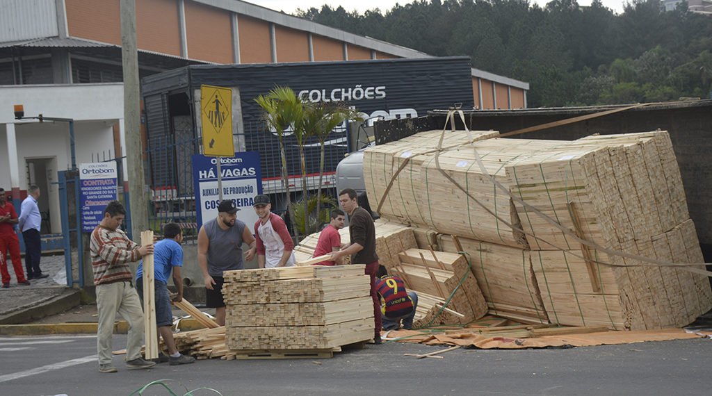 Caminhão carregado de madeira tomba ao tentar entrar em empresa